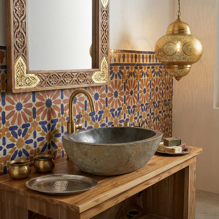 Lavatório em pedra de rio numa casa de banho oriental, assente numa consola de madeira, combinado com torneiras em latão, azulejos em mosaico e iluminação acolhedora