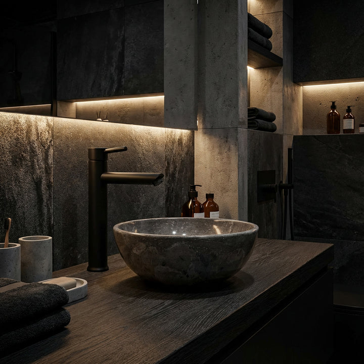 Lavatório redondo de mármore sobre um móvel de madeira escura numa casa de banho moderna em estilo spa, com torneiras pretas e iluminação indireta