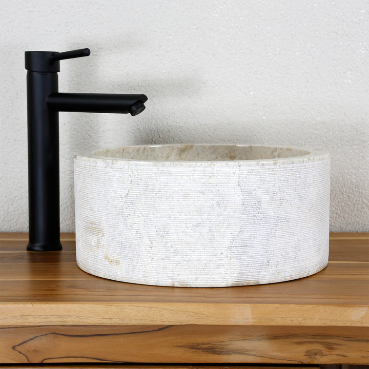 Lavatório redondo de pedra natural clara com uma textura de linhas finas, combinado com uma torneira de pé preta.