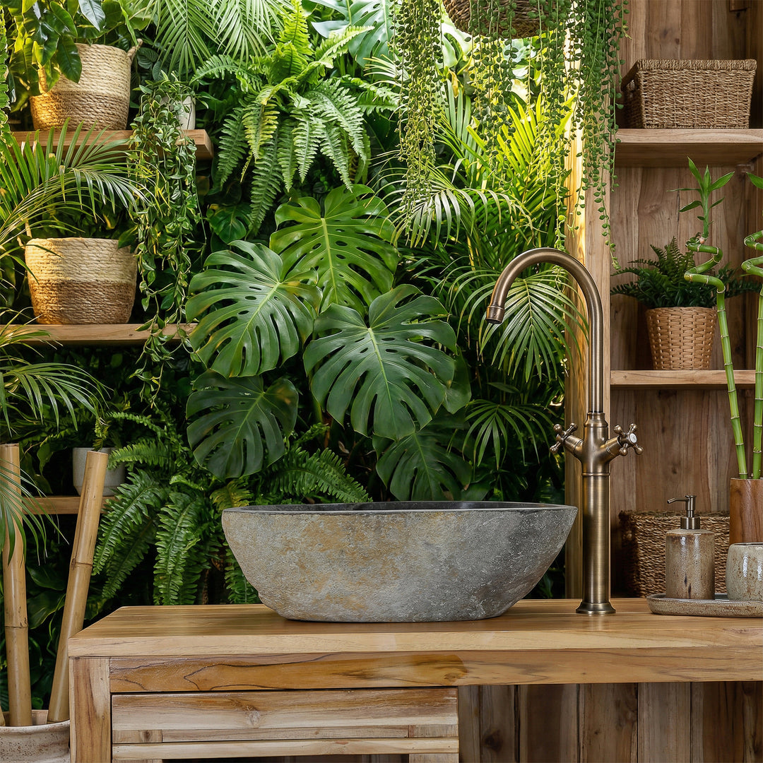 Lavatório de pedra de rio na casa de banho spa verde, assente numa bancada de madeira, combinado com torneiras em latão e um ambiente repleto de plantas