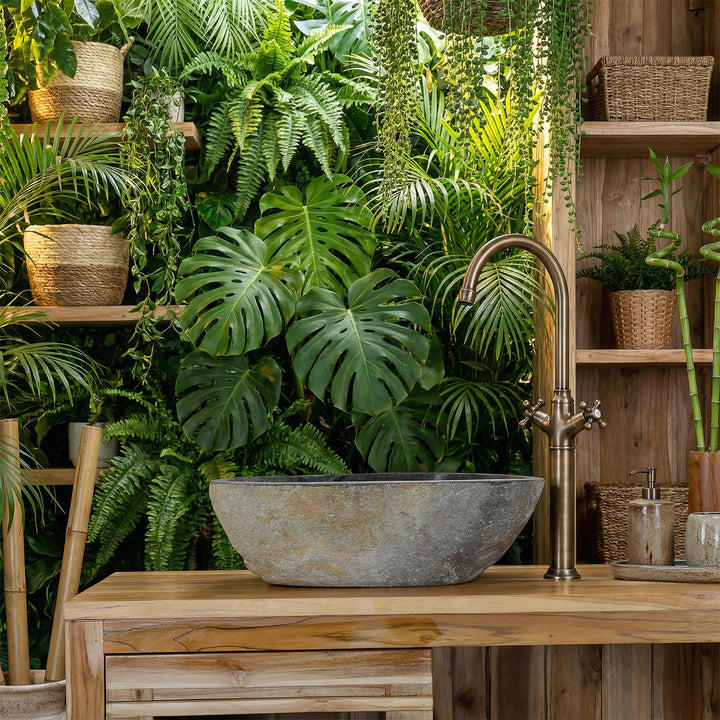 Lavatório de pedra de rio na casa de banho spa verde, assente numa bancada de madeira, combinado com torneiras em latão e um ambiente repleto de plantas