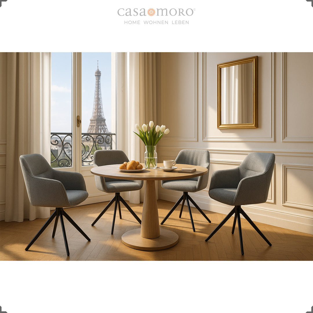 Quatro cadeiras estofadas com braços, giratórias a 360°, em tom cinzento, dispostas em torno de uma mesa redonda de madeira numa elegante sala de jantar com vista para a Torre Eiffel