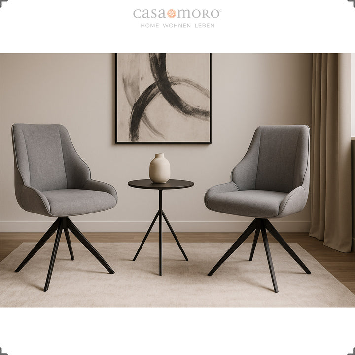 Duas cadeiras de sala de jantar giratórias a 360°, em cinzento com estrutura metálica preta, junto a uma mesa de apoio redonda, numa sala de estar moderna e com decoração clara