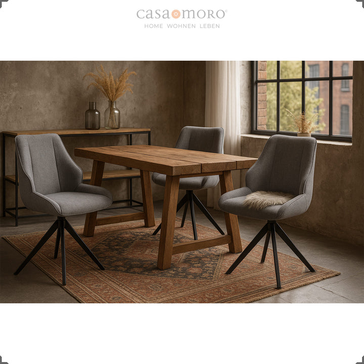 Três cadeiras de sala de jantar giratórias a 360° em cinzento, com estrutura metálica preta, dispostas em torno de uma mesa de madeira num ambiente moderno de loft, com tapete e decoração