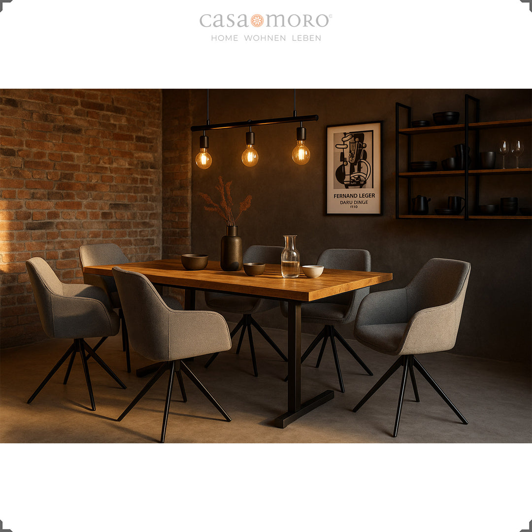 Seis cadeiras estofadas com braços, giratórias a 360°, em tom cinzento, dispostas em torno de uma mesa de madeira numa sala de jantar moderna com parede de tijolo e iluminação acolhedora