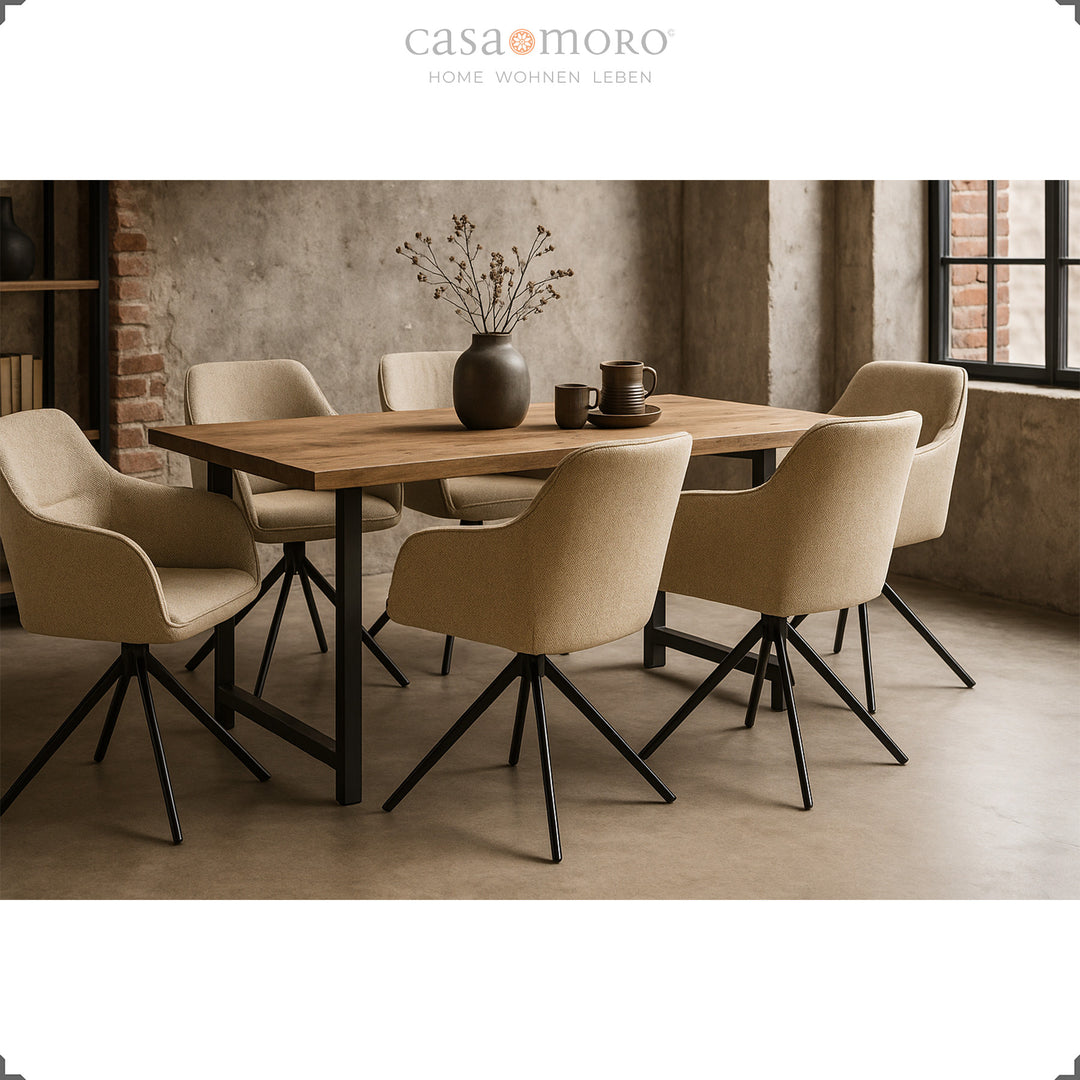Seis cadeiras estofadas com braços, em bege, que giram 360°, dispostas em torno de uma mesa de madeira numa sala de jantar moderna com paredes de betão e estrutura de metal preta