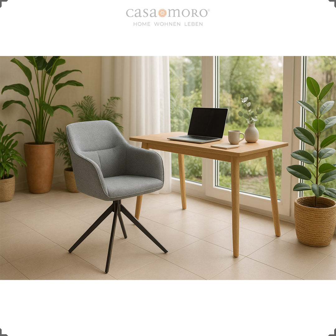 Cadeira estofada giratória a 360°, com braços, na cor cinzenta, junto a uma mesa de madeira com um computador portátil, rodeada por plantas e grandes janelas, num ambiente doméstico luminoso
