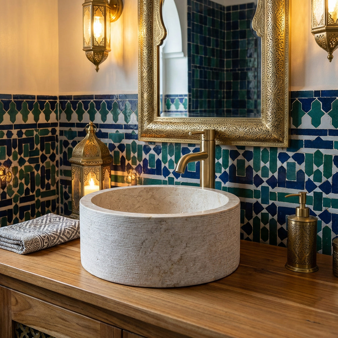 Lavatório redondo em mármore sobre uma consola de madeira, apresentado de forma cénica numa casa de banho de estilo oriental com azulejos em mosaico e detalhes em latão.