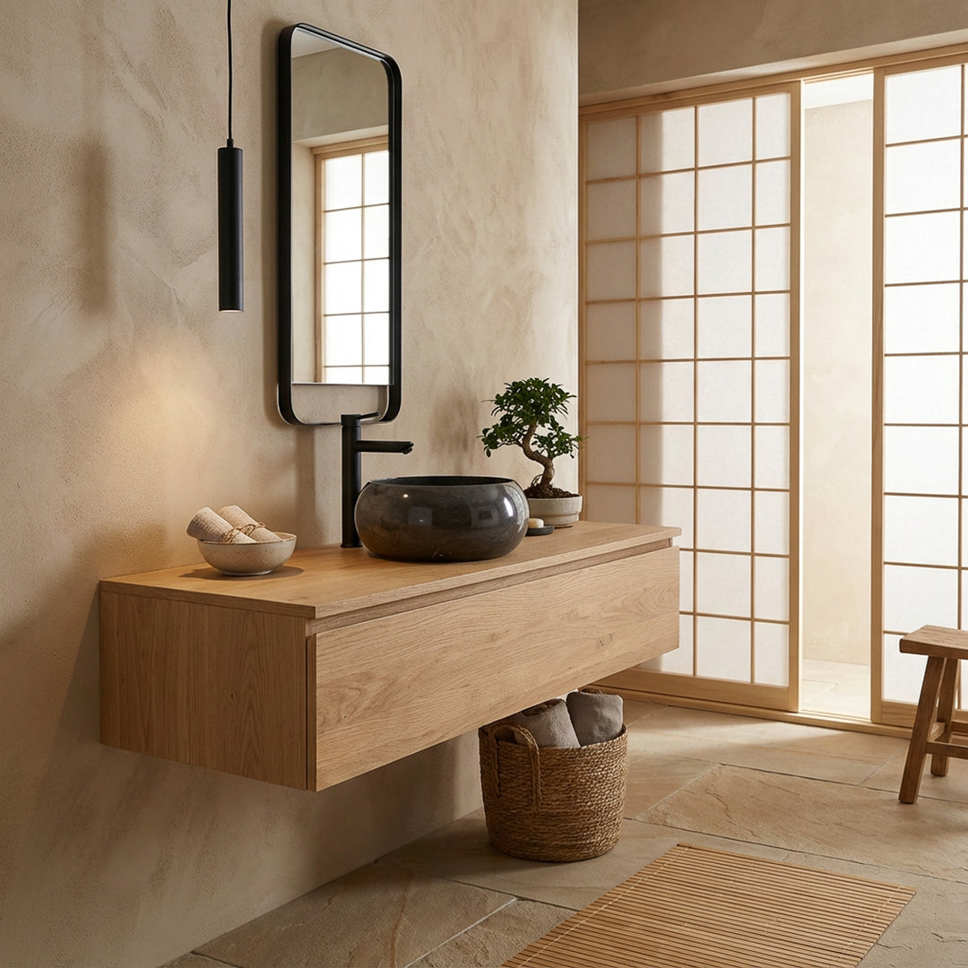 Lavatório redondo em pedra sobre um móvel suspenso de madeira numa casa de banho de inspiração japonesa, combinado com torneiras pretas, um espelho com moldura de madeira e uma suave luz natural