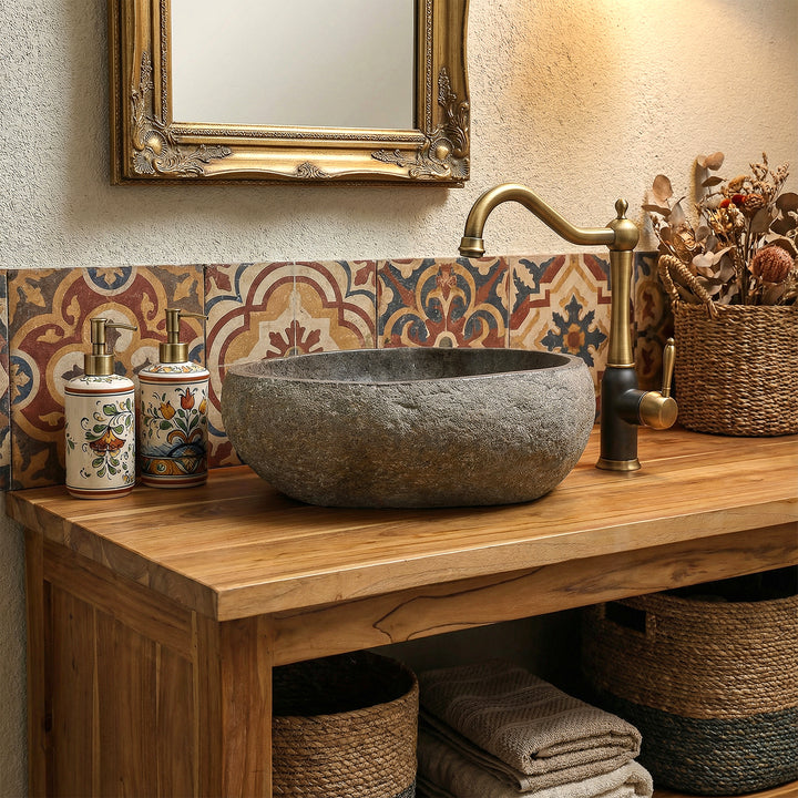 Lavatório em pedra natural numa casa de banho de estilo boho acolhedor, sobre um móvel de casa de banho em madeira, combinado com torneiras em latão e azulejos estampados