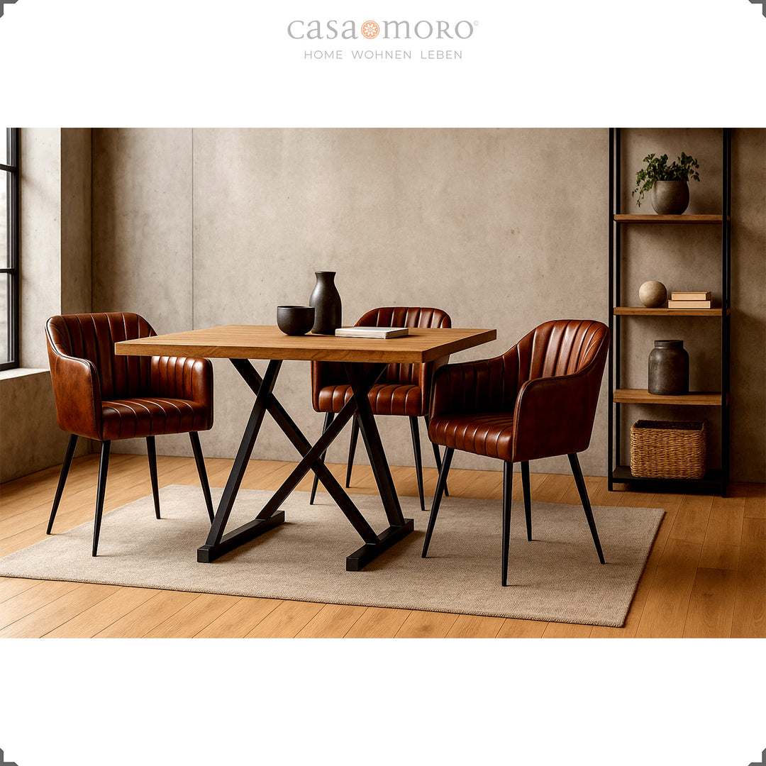 Três poltronas de couro castanho antigo com costura vertical, dispostas em torno de uma mesa de madeira com estrutura de metal preta, numa sala de jantar moderna com iluminação acolhedora e decoração minimalista.