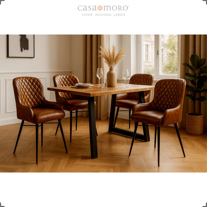 Quatro cadeiras de couro castanho antigo com costura em losango, dispostas em torno de uma mesa de madeira numa elegante sala de jantar com piso em parquet, revestimento de parede claro e decoração natural.