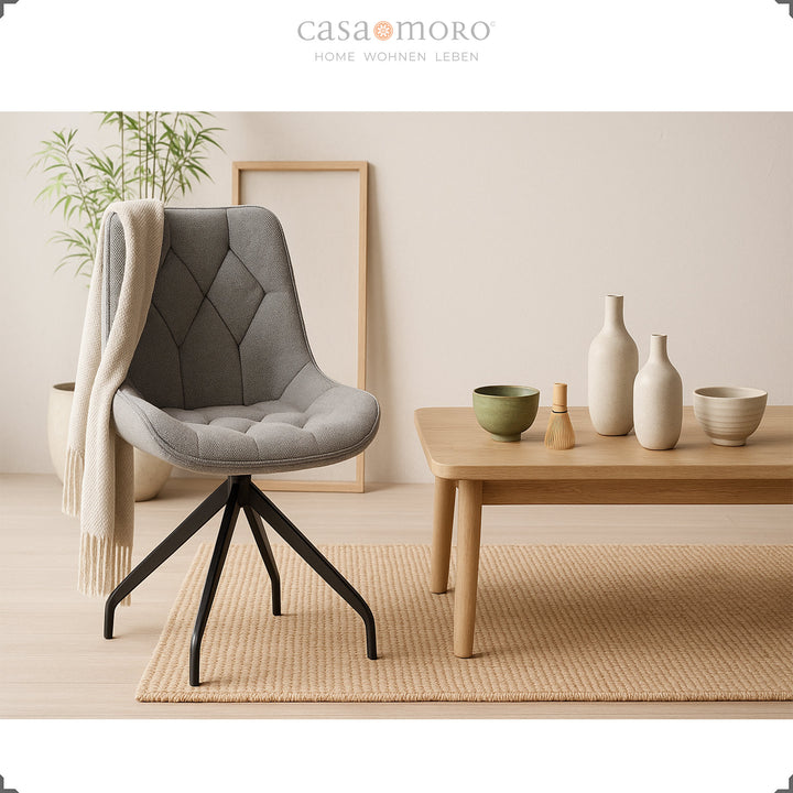 Cadeira estofada cinzenta com rotação de 360° e estrutura metálica preta – cadeira de destaque moderna junto a uma mesa de madeira com decoração em cerâmica num ambiente doméstico natural