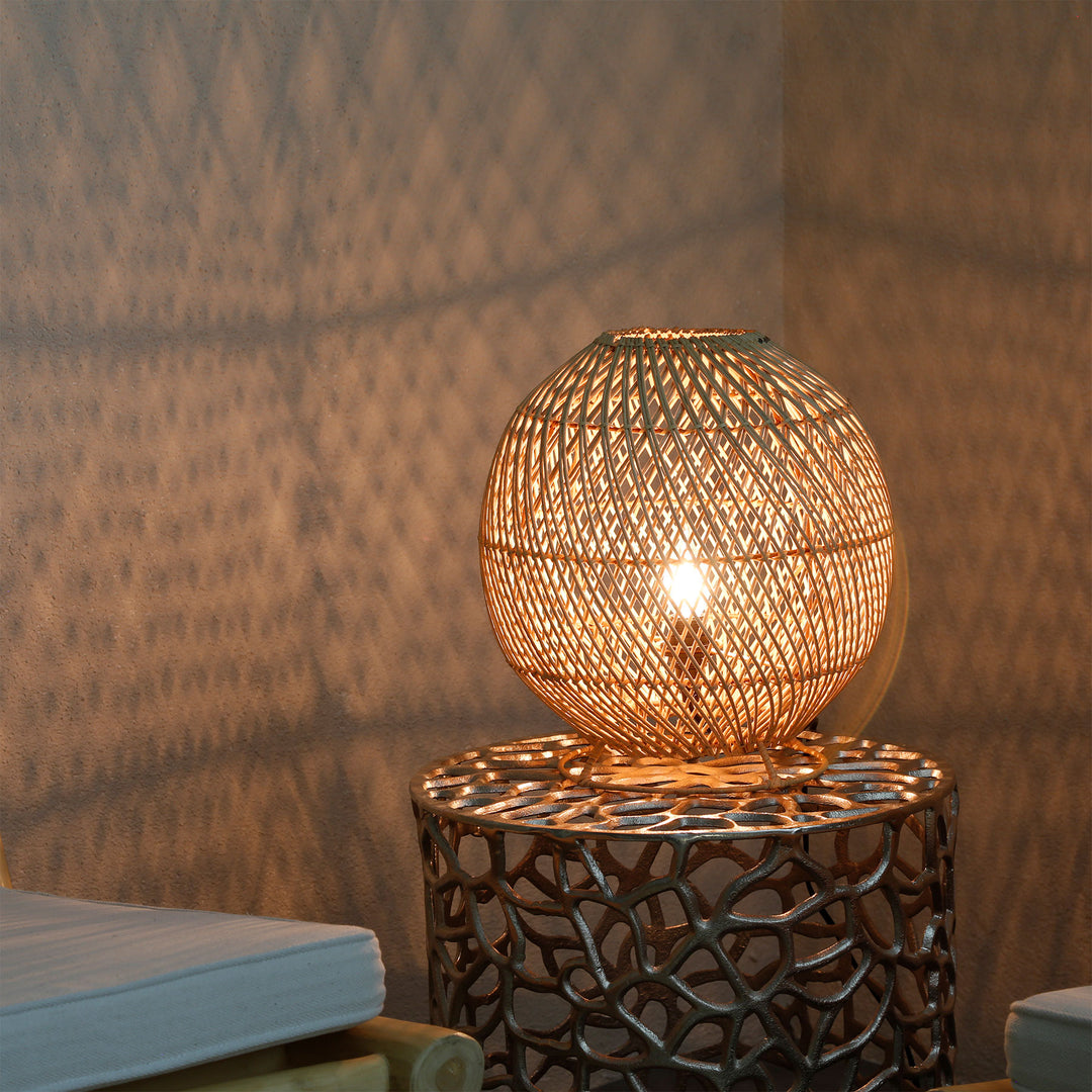 Candeeiro redondo de rattan sobre uma mesinha de apoio na sala de estar, com um delicado padrão de luz na parede