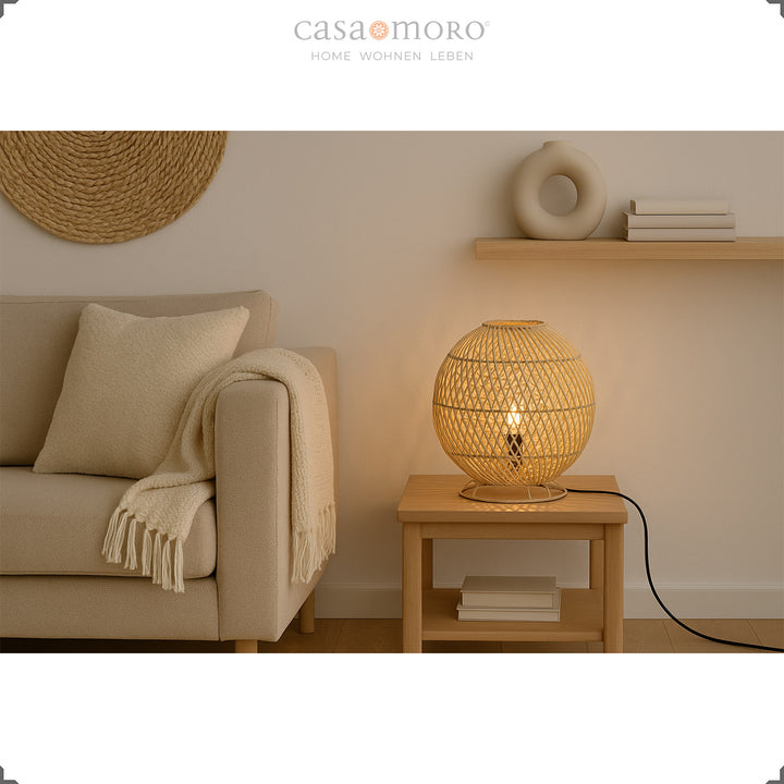 Candeeiro de mesa redondo em rattan sobre uma mesinha de apoio ao lado do sofá, luz acolhedora e decoração natural
