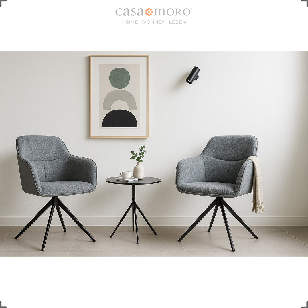 Duas cadeiras estofadas com braços, em cinzento, que rodam 360°, ao lado de uma mesa de apoio redonda, numa sala de estar moderna com decoração de parede clara
