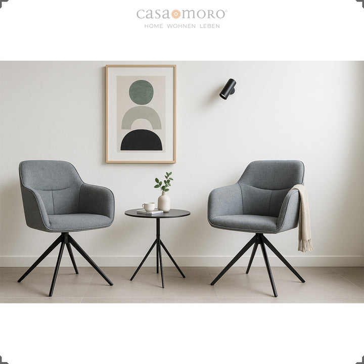 Duas cadeiras estofadas com braços, em cinzento, que rodam 360°, ao lado de uma mesa de apoio redonda, numa sala de estar moderna com decoração de parede clara