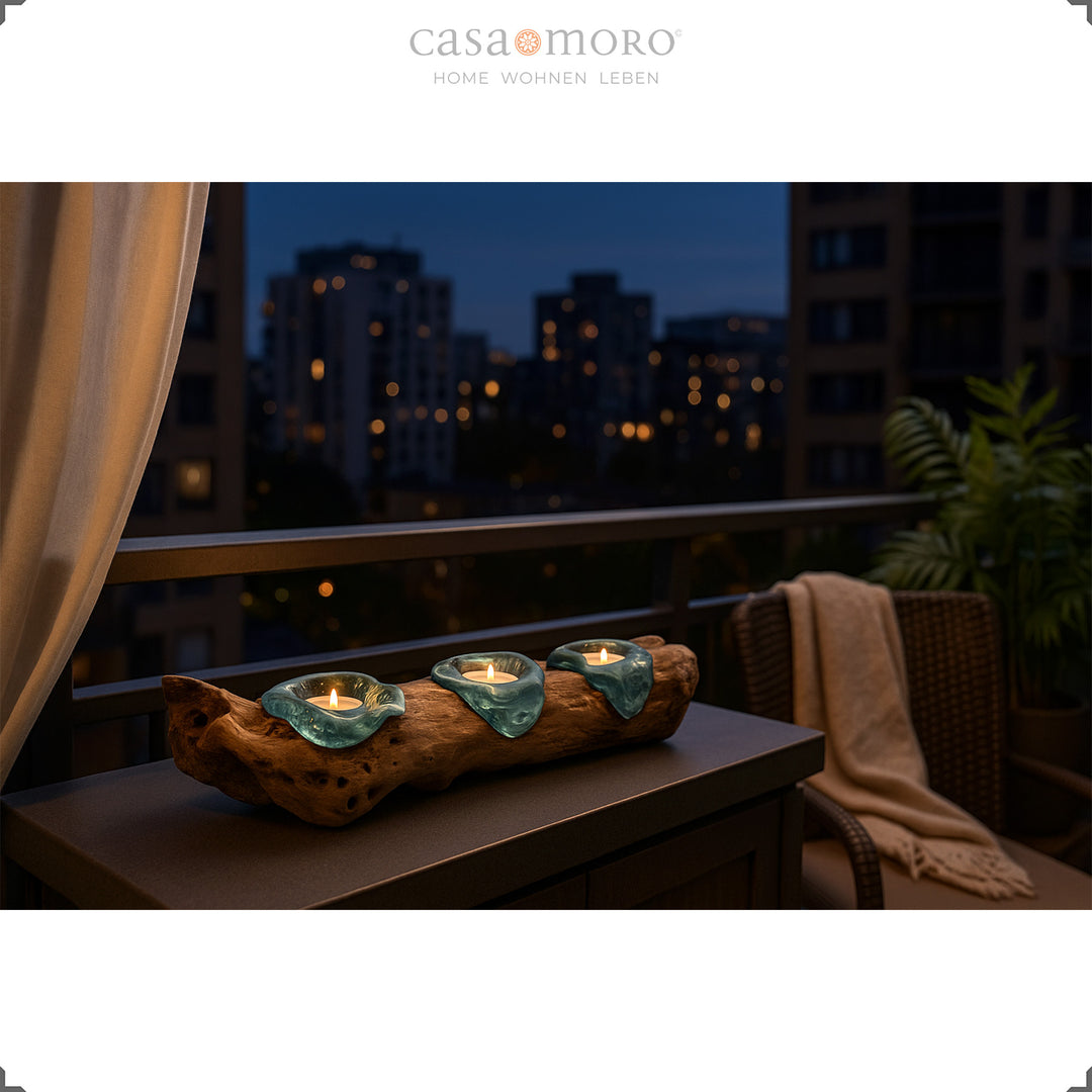Conjunto de três castiçais para velas de chá em vidro e madeira de raiz numa varanda à noite, com vista para a cidade e um confortável banco