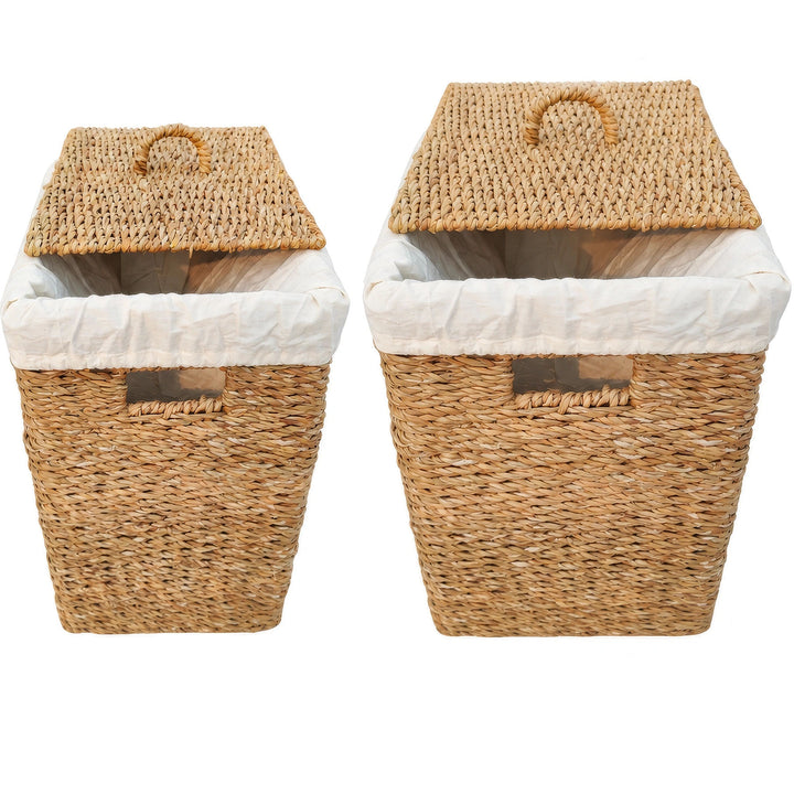 Dois cestos retangulares para a roupa suja, feitos de erva-do-mar, com 50 e 90 litros de capacidade, com inserções de tecido de cor clara e tampas colocadas na diagonal.
