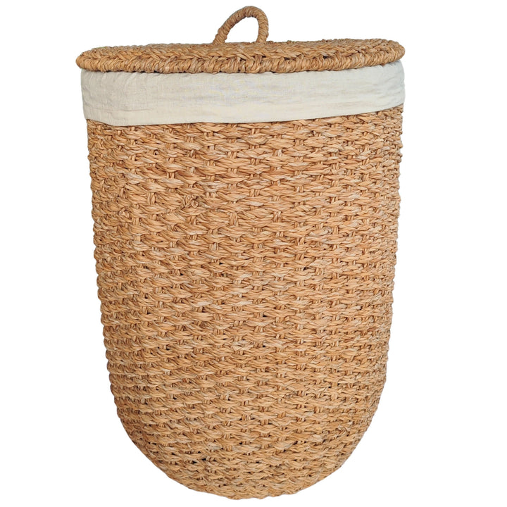 Cesto de roupa suja aberto, em erva-do-mar de cor natural, com um revestimento em tecido claro e uma tampa encostada lateralmente.