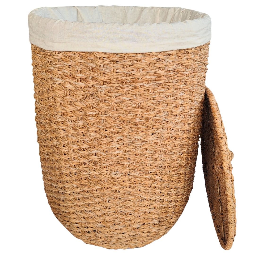 Cesto de roupa suja aberto, em erva-do-mar de cor natural, com um revestimento em tecido claro e uma tampa encostada lateralmente.