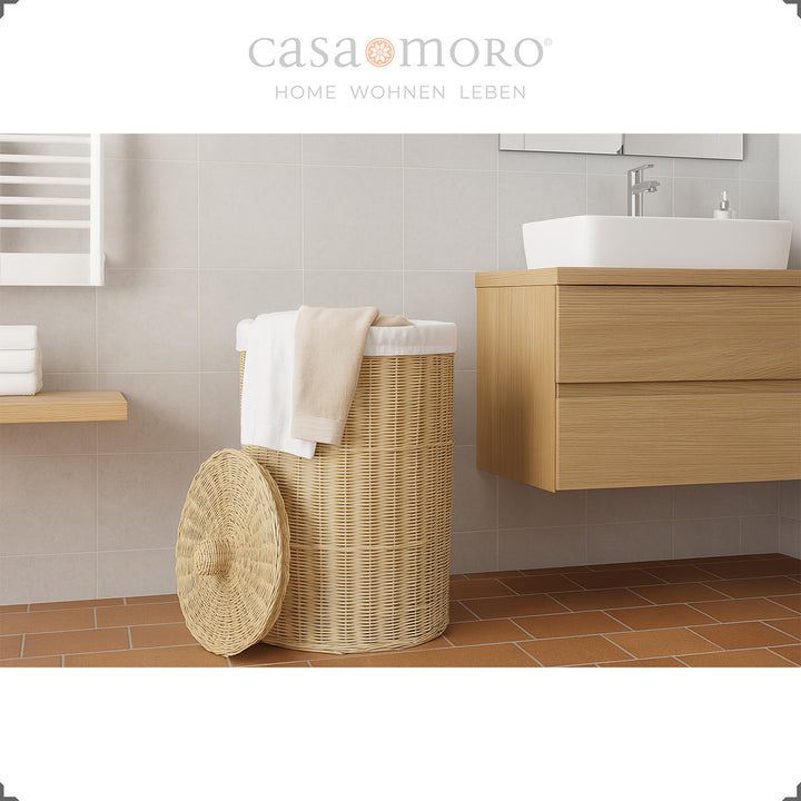 Cesto de roupa suja trançado em cor natural com tampa, decorado com uma toalha branca na casa de banho