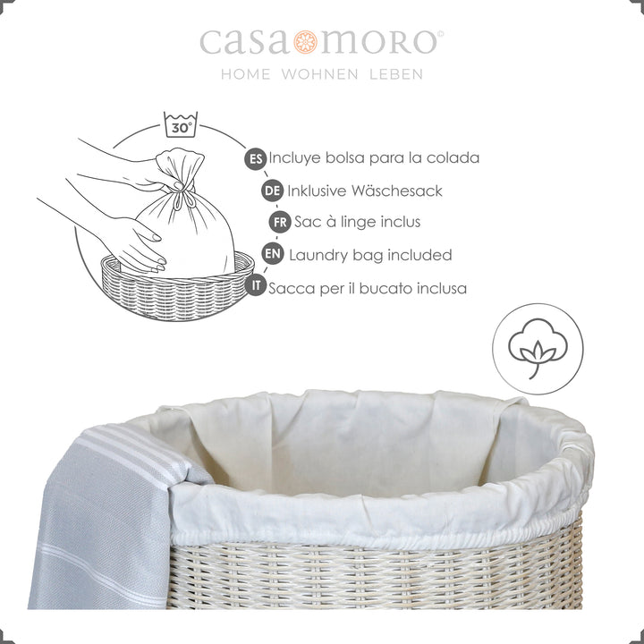 Cesto de roupa suja em rattan caiado de branco com forro em algodão claro, decorado com uma toalha de banho