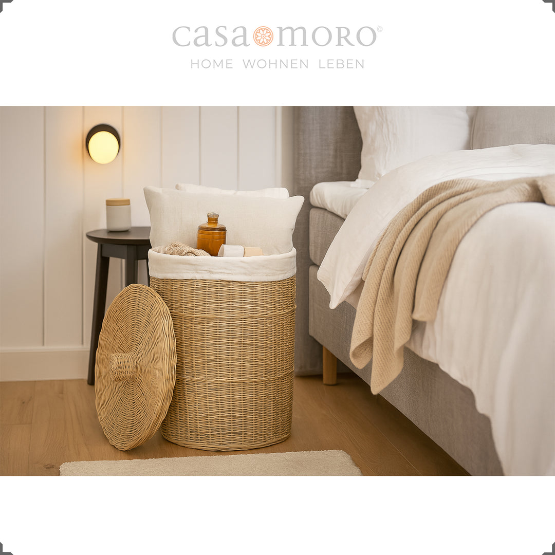 Cesto de roupa suja redondo em rattan com tampa no quarto, cheio de almofadas, cobertores e produtos de higiene pessoal