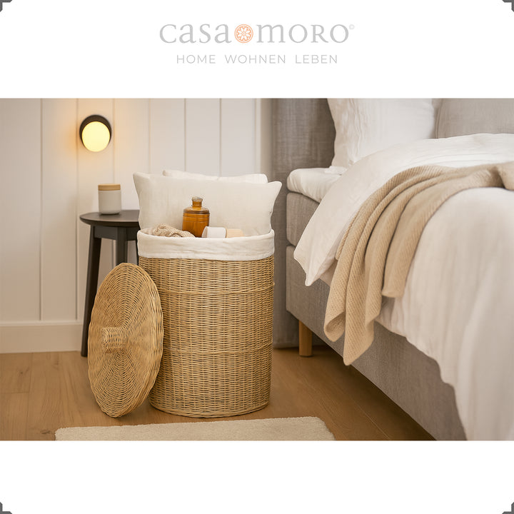 Cesto de roupa suja redondo em rattan com tampa no quarto, cheio de almofadas, cobertores e produtos de higiene pessoal