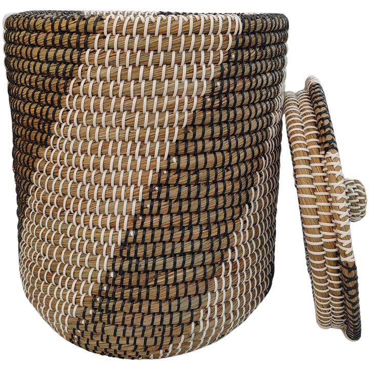Cesto da roupa suja em erva-do-mar, nas cores natural, preta e branca, com um volume de cerca de 40 litros e tampa encostada lateralmente.