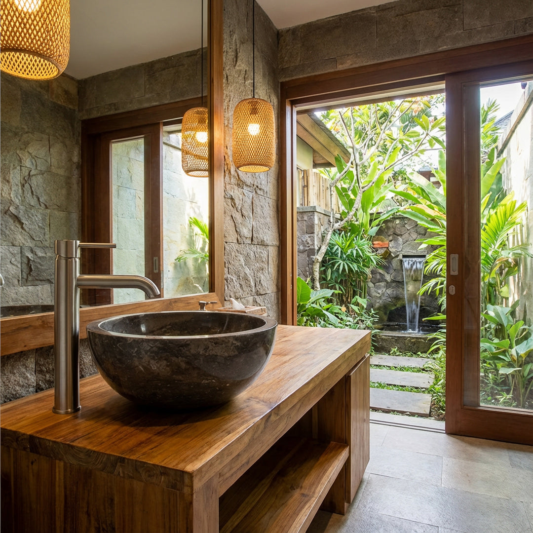 Lave-mãos redondo em mármore escuro sobre um lavatório de madeira com torneira em aço inoxidável, numa casa de banho tipo spa aberta com vista para o jardim